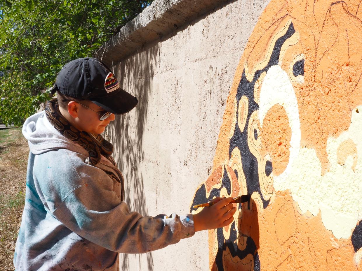 A woman paints a snake while holding a snake on her shoulder