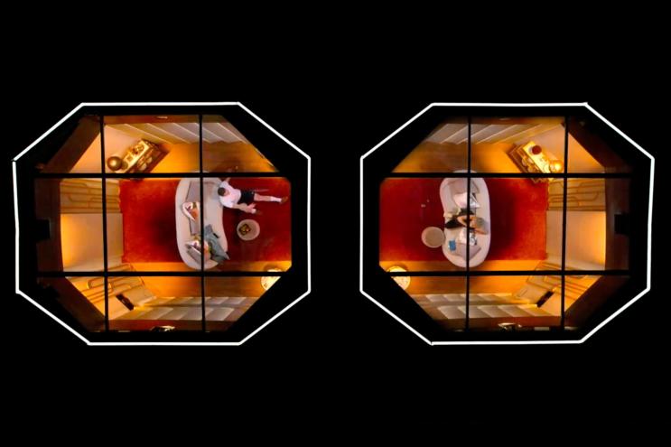 A man and woman seen from above in separate rooms, talking to one another through a wall.