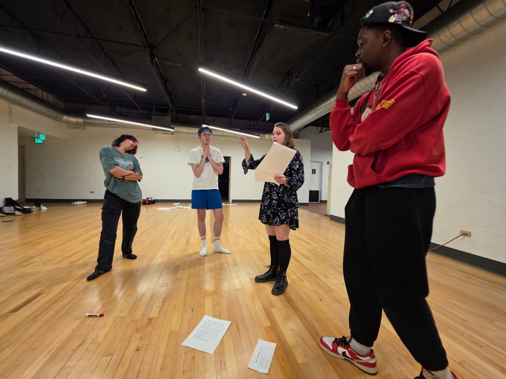 Theater artists talk together in a rehearsal space.