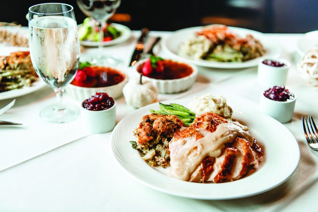 A plate of sliced turkey with gravy, stuffing and mashed potatoes backdropped by a Thanksgiving spread from Eddie Merlot's