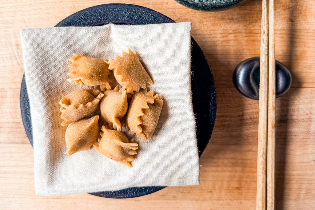 A pile of agnolotti on a cloth napkin with chopsticks.