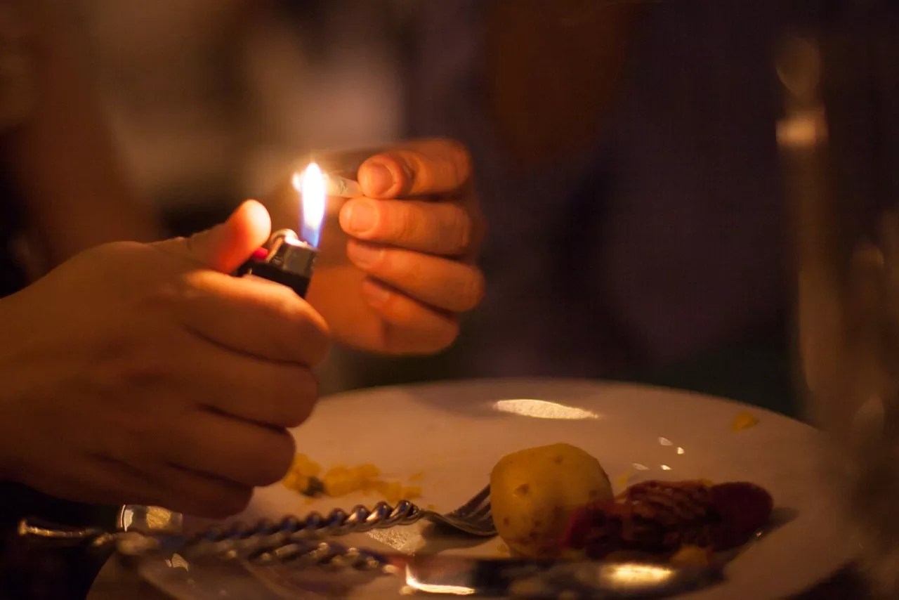 person lights joint over dinner plate