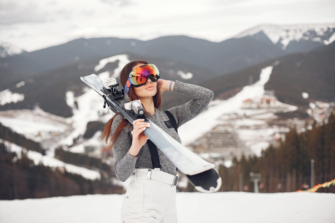 Young brunette woman holding skis in the snowy mountains.
