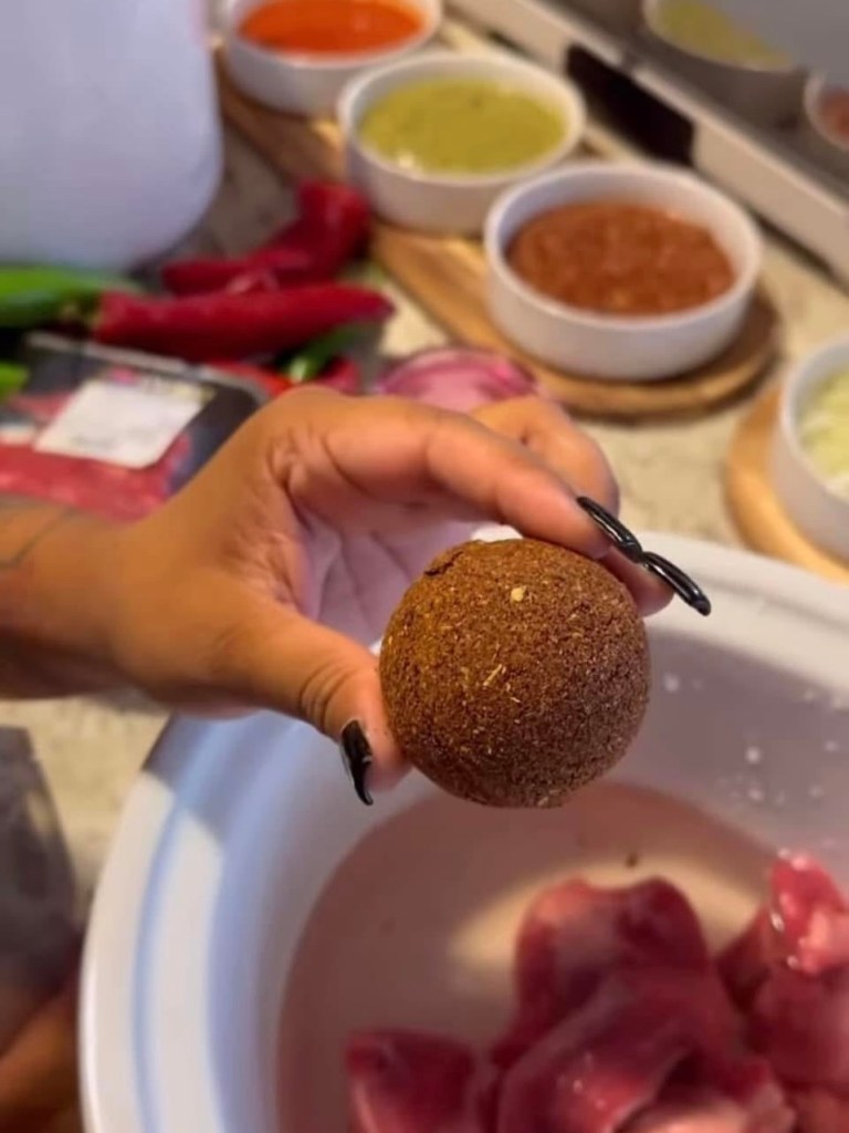 A spherical Bombitas spice bomb held over a crockpot filled with water and meat