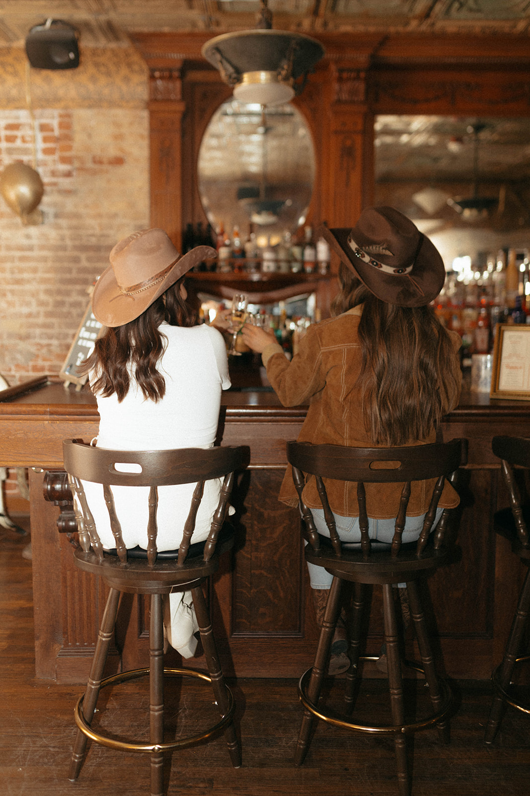 Two women wearing hats by Gem Hats at bar at Urban Cowboy in Denver