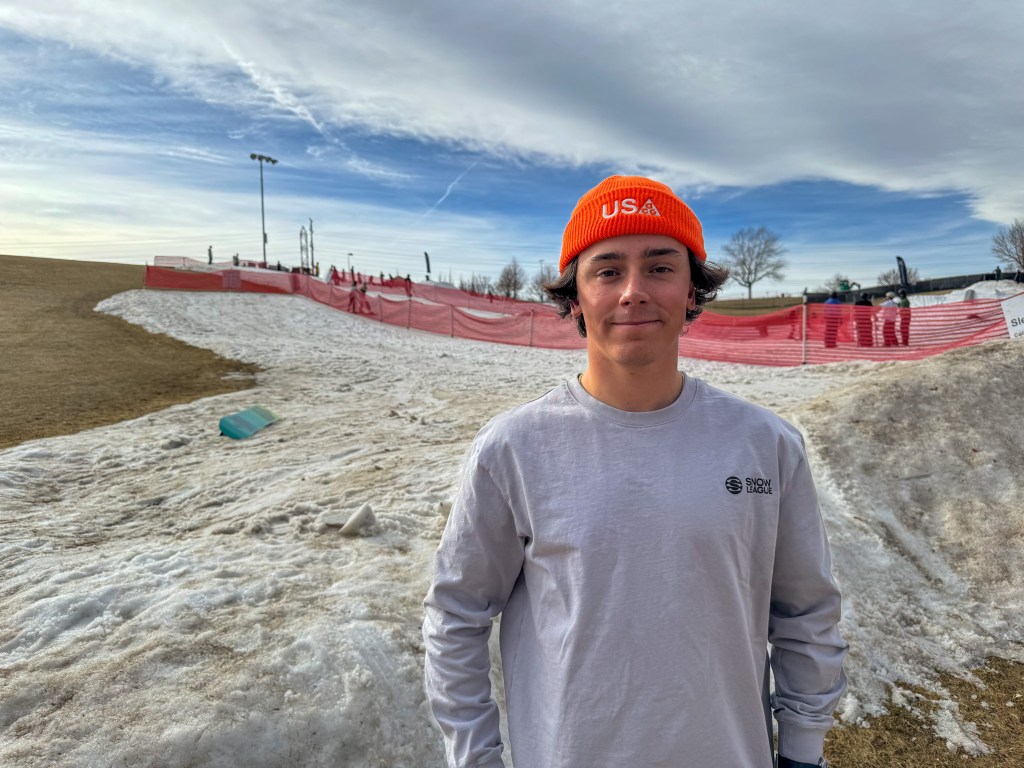 Chase Blackwell poses in front of the snow hill at Ruby Hill Rail Yard. He's wearing a bright orange beanie that says USA.