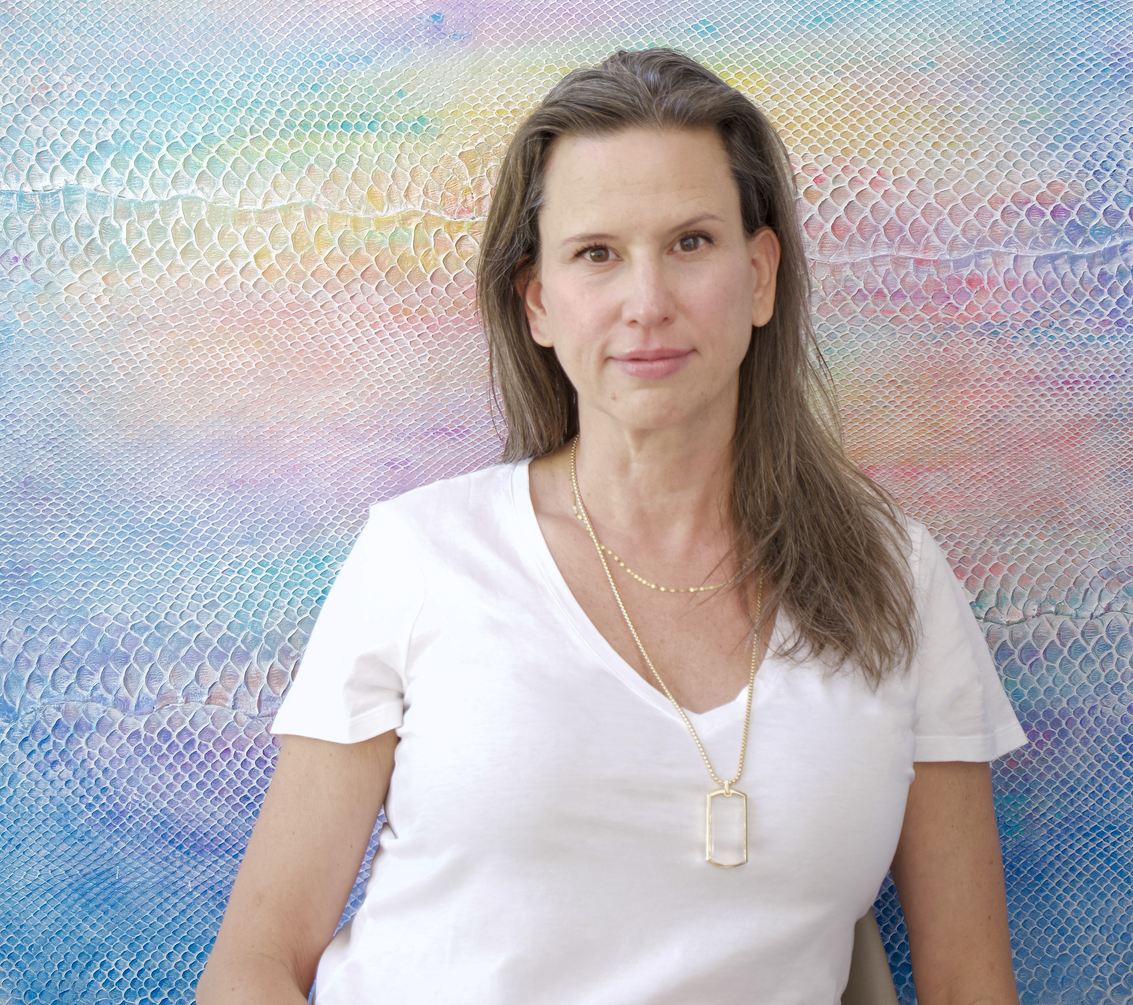 Artist Laura Shape stands in front of a colorful painting made of the skin of an invasive python species.