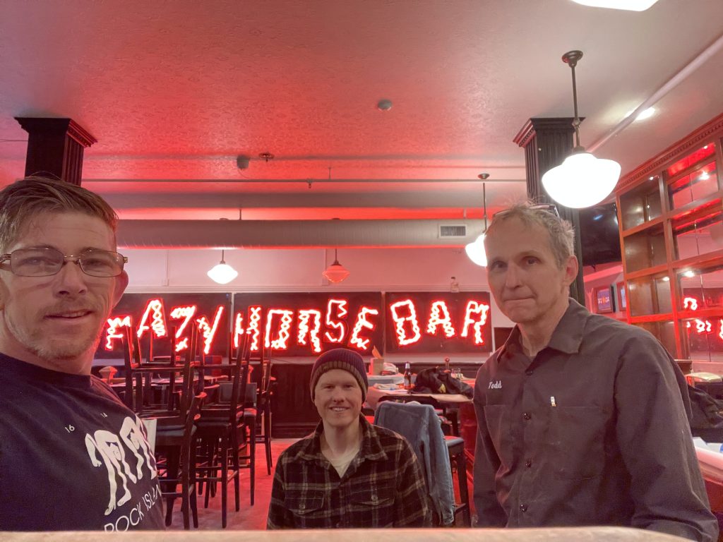 Three men pose in front of a neon sign