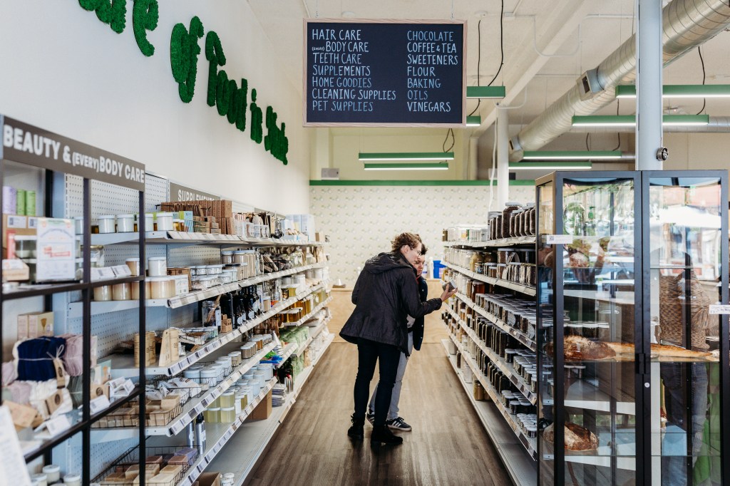 Customers in a Nude Foods aisle stocked with body care products and baking goods