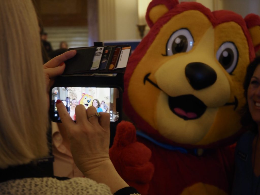 People take a picture of a pink bear mascot
