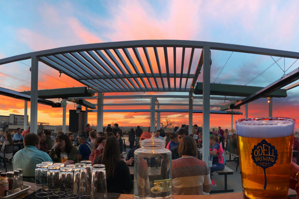 People seated on the Odell rooftop, with the sunset and Sloan's Lake in the backdrop