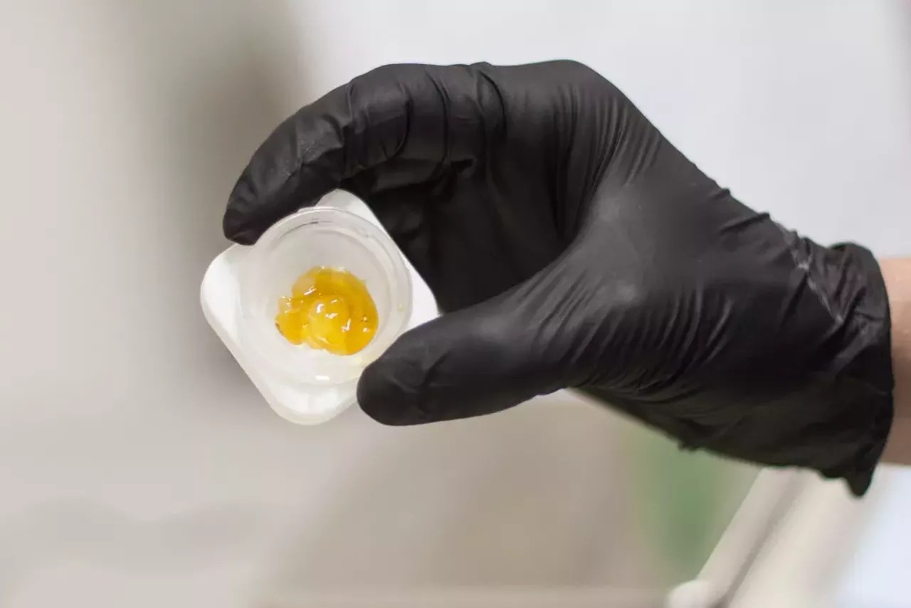 A cannabis extraction worker holds a jar of THC wax.