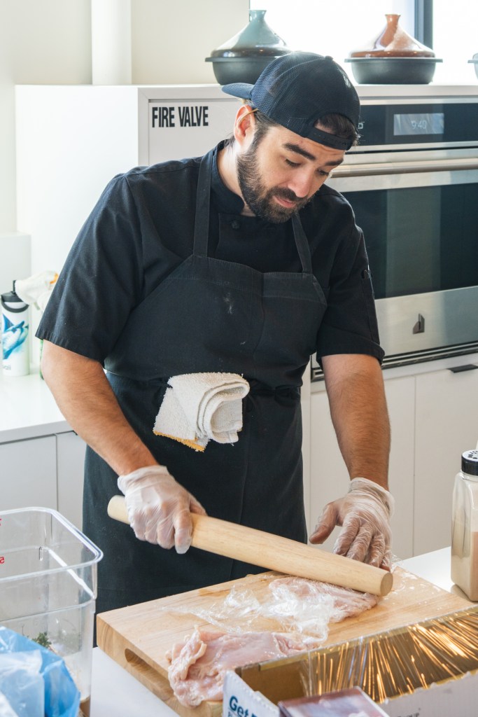 chef using rolling pin to pound chicken breasts