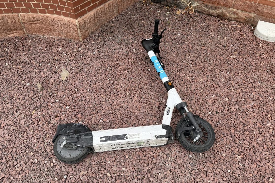 a bird scooter lies on the gravel next to the sidewalk in downtown denver