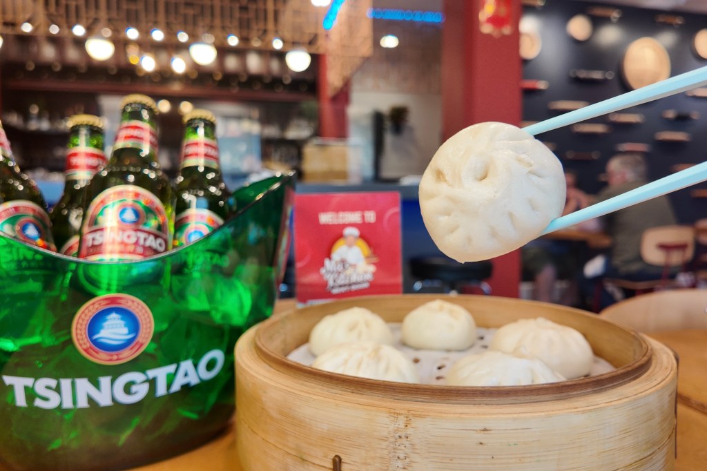 Chopsticks holding up a steamed bun from Ma’s Kitchen, with a bucket of Tsingtao beer in the backdrop
