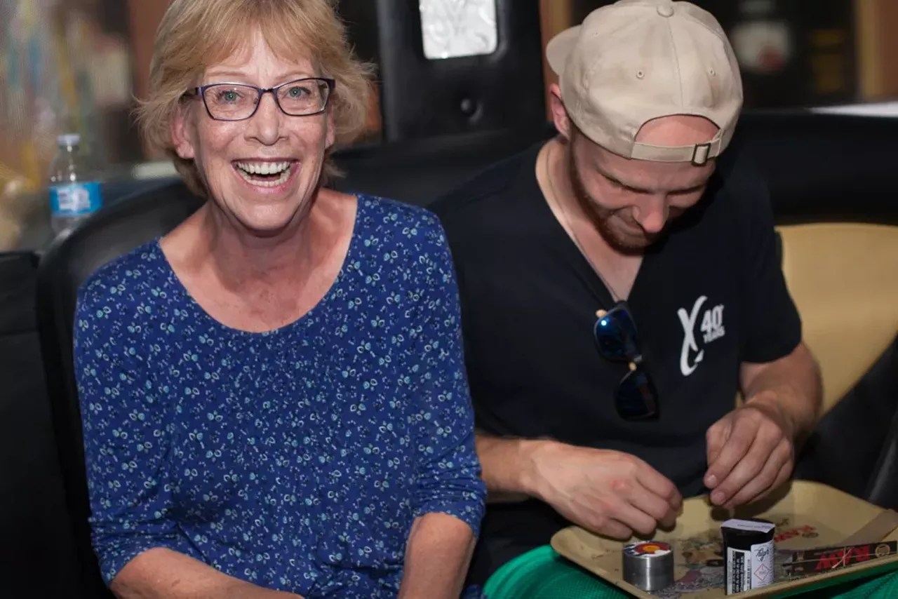 Man rolls joint inside of a cannabis consumption bus as a woman sits nexts to him, smiling
