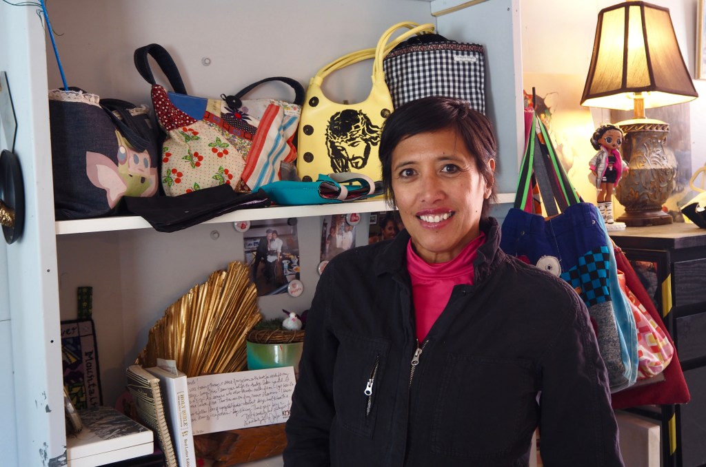 A person stands in front of a shelf of purses
