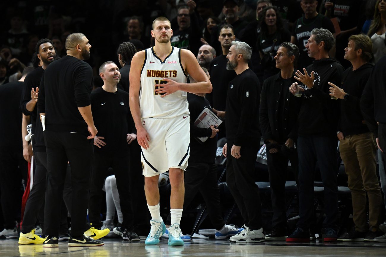 Denver Nuggets star Nikola Jokic stands surrounded by the Nuggets coaching staff during a game