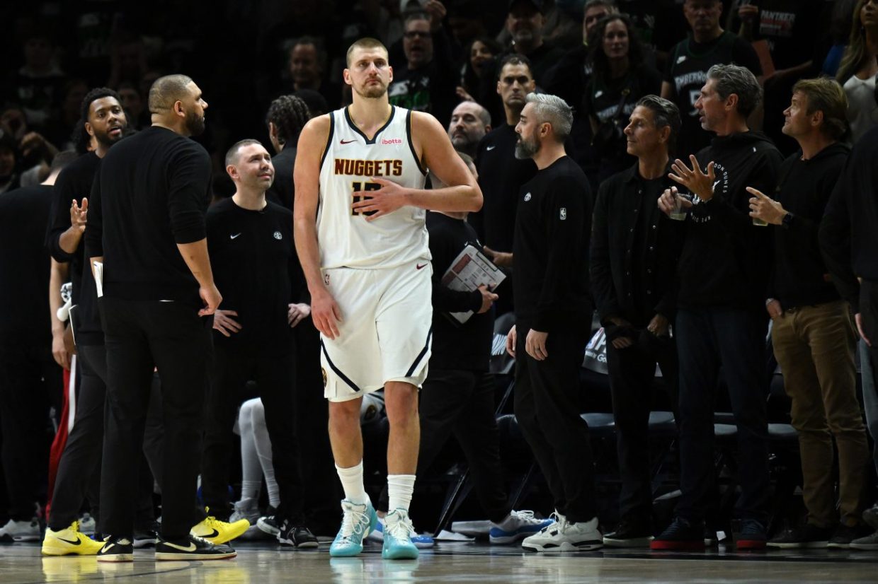 Denver Nuggets star Nikola Jokic stands surrounded by the Nuggets coaching staff during a game