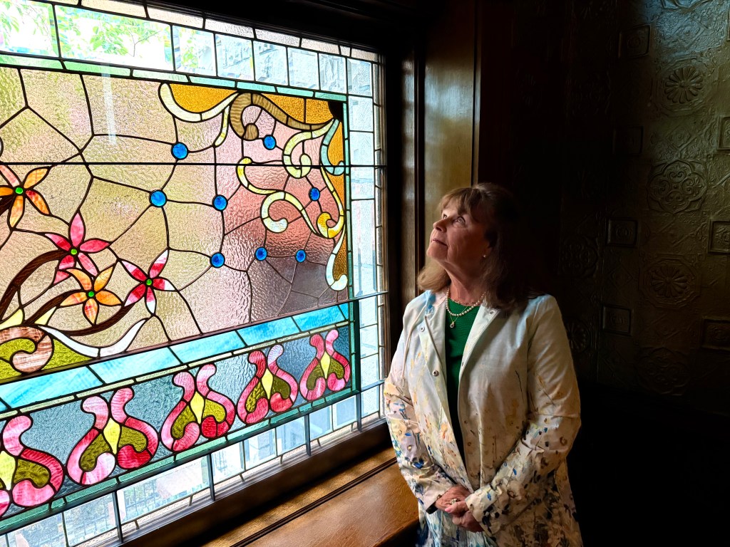 Jane Watkins next to the window Watkins Stained Glass restored at the Molly Brown House Museum.