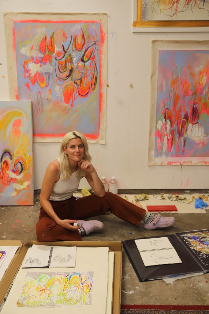 An artist sits on the floor with her work