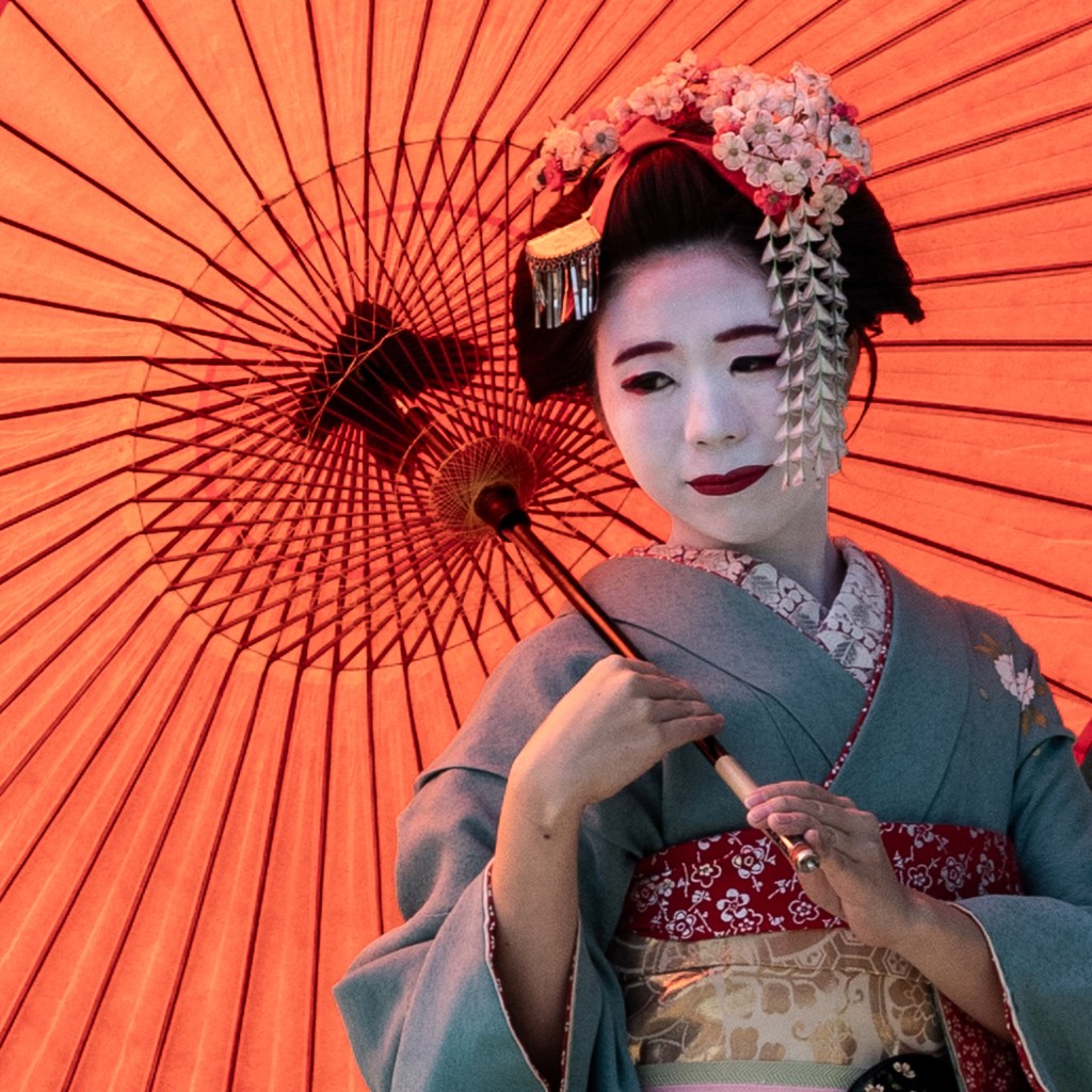 A photograph of a geisha holding an orange umbrella