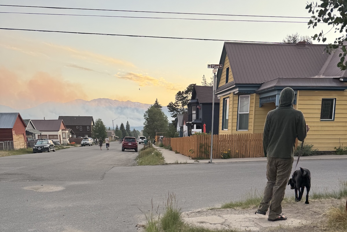 A man walks his dog in his neighborhood as the Willow fire burns in the background.
