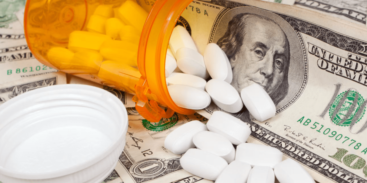 A prescription bottle and pills sit next to $100 bills