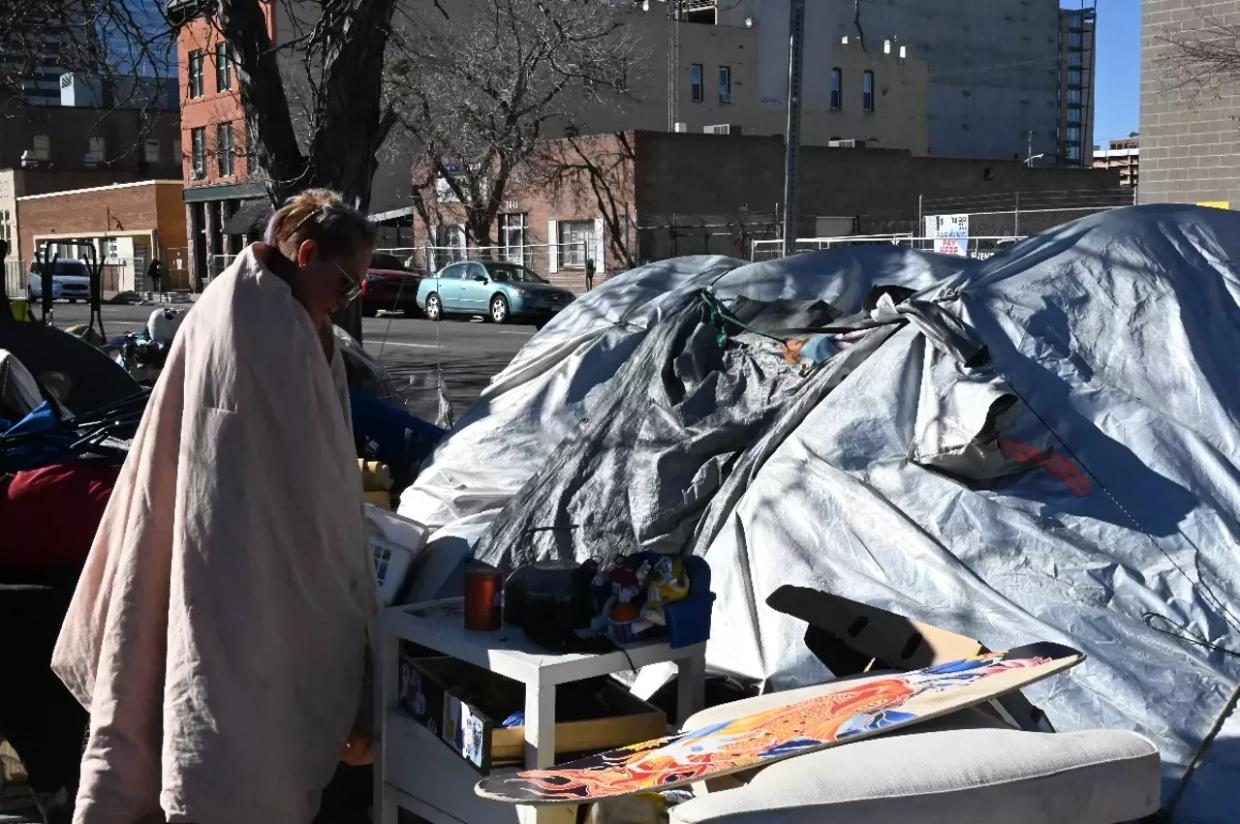 A homeless resident stands outside her tent at the corner of 21st and Curtis streets, just outside the U.S. Post Office., in late 2023.
