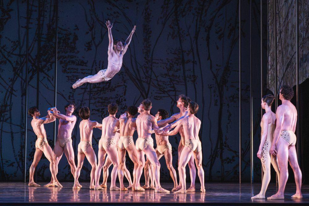A ballerina soars through the air while others prepare to catch them