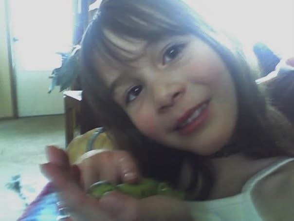 A closeup of Cass Ivey as a young girl. She's holding and petting what appears to be a green alligator toy.