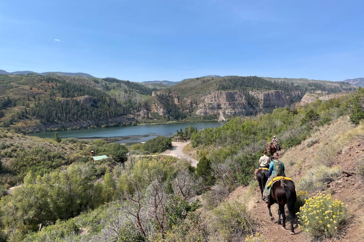A group of women on horseback, backdropped by mountain and lake views