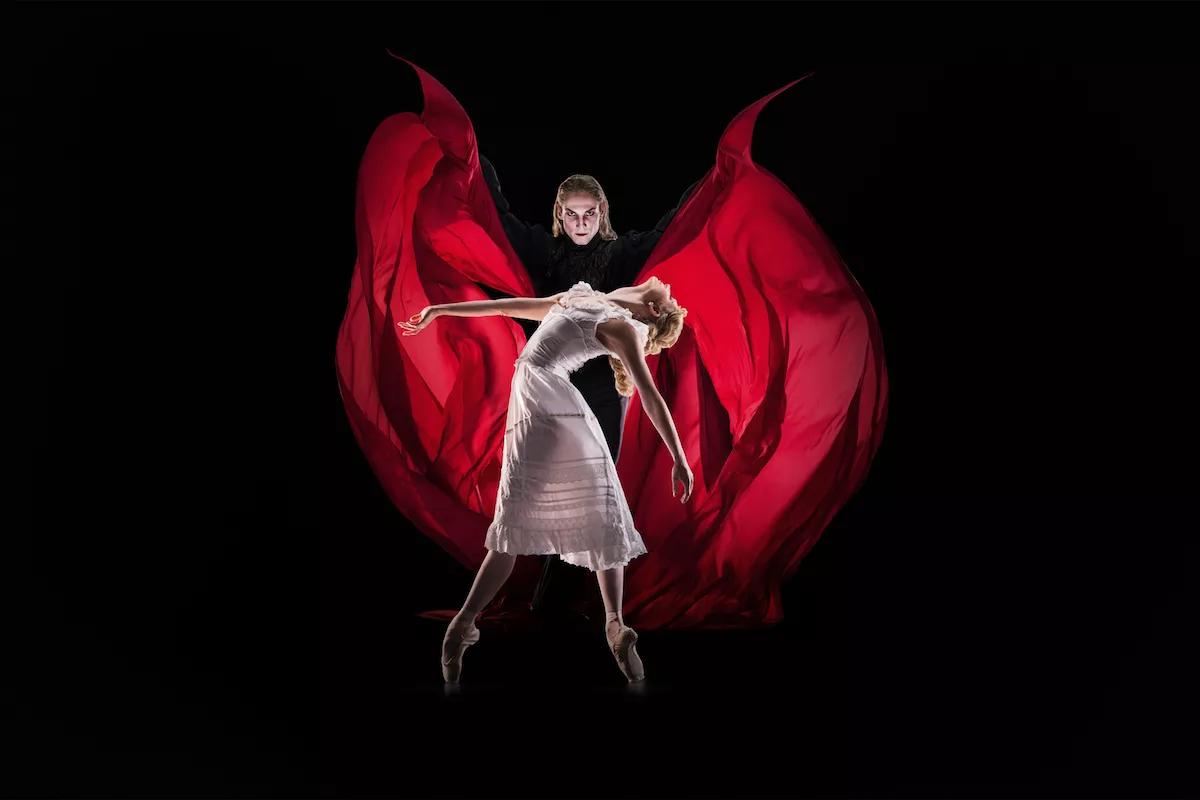 A man wearing a red cape stands behind a woman.