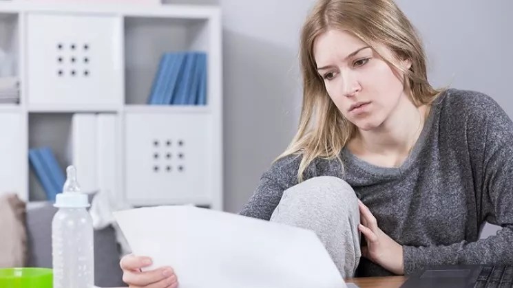 A blonde woman gazes at a document with a perturbed expression.