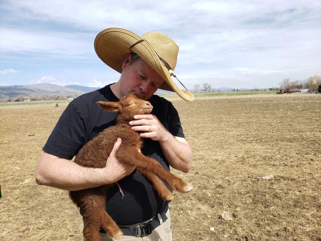 man in hat holding lamb on farm