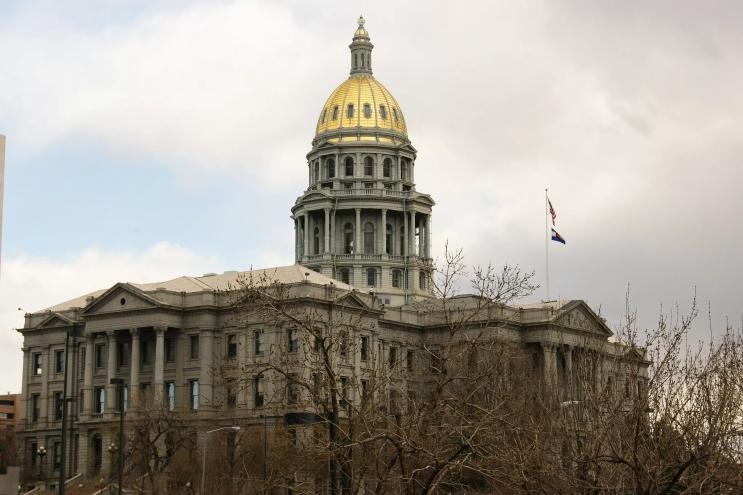 The Colorado state capitol's gold dome in the foreground of a cloudy sky.