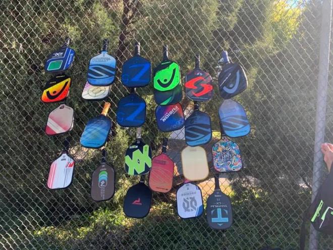 Colorful pickleball paddles stacked in a fence.