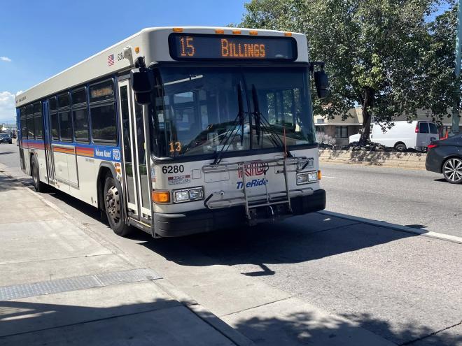 A bus trundles along a day-lit street on Colfax Avenue in Denver.