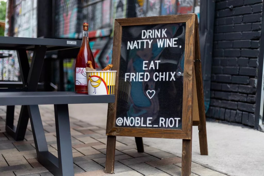 bottle of wine and bucket of fried chicken next to a sign
