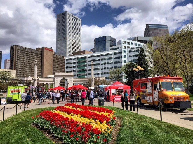 downtown skyline behind food truck parked near a flower garden