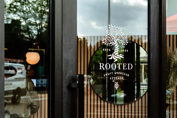 a black sign that says "rooted" behind a glass door