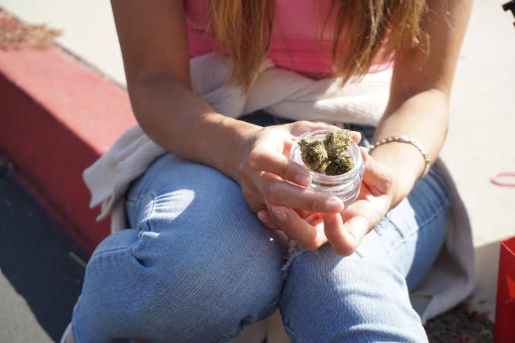 A woman holds a glass jar of cannabis flower.