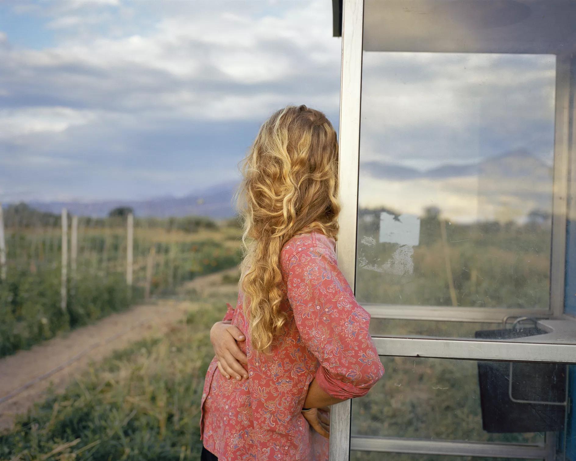 blonde woman leaning on a window looking out at the countryside
