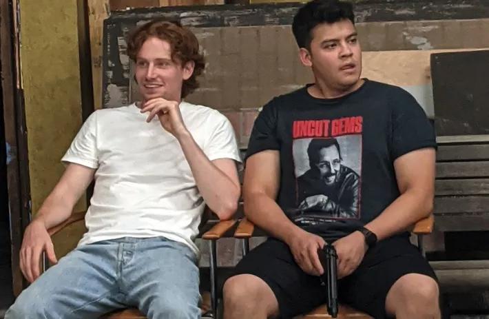 a ginger boy in a white t shirt and a man with black hair in a black shirt holding a fake gun.