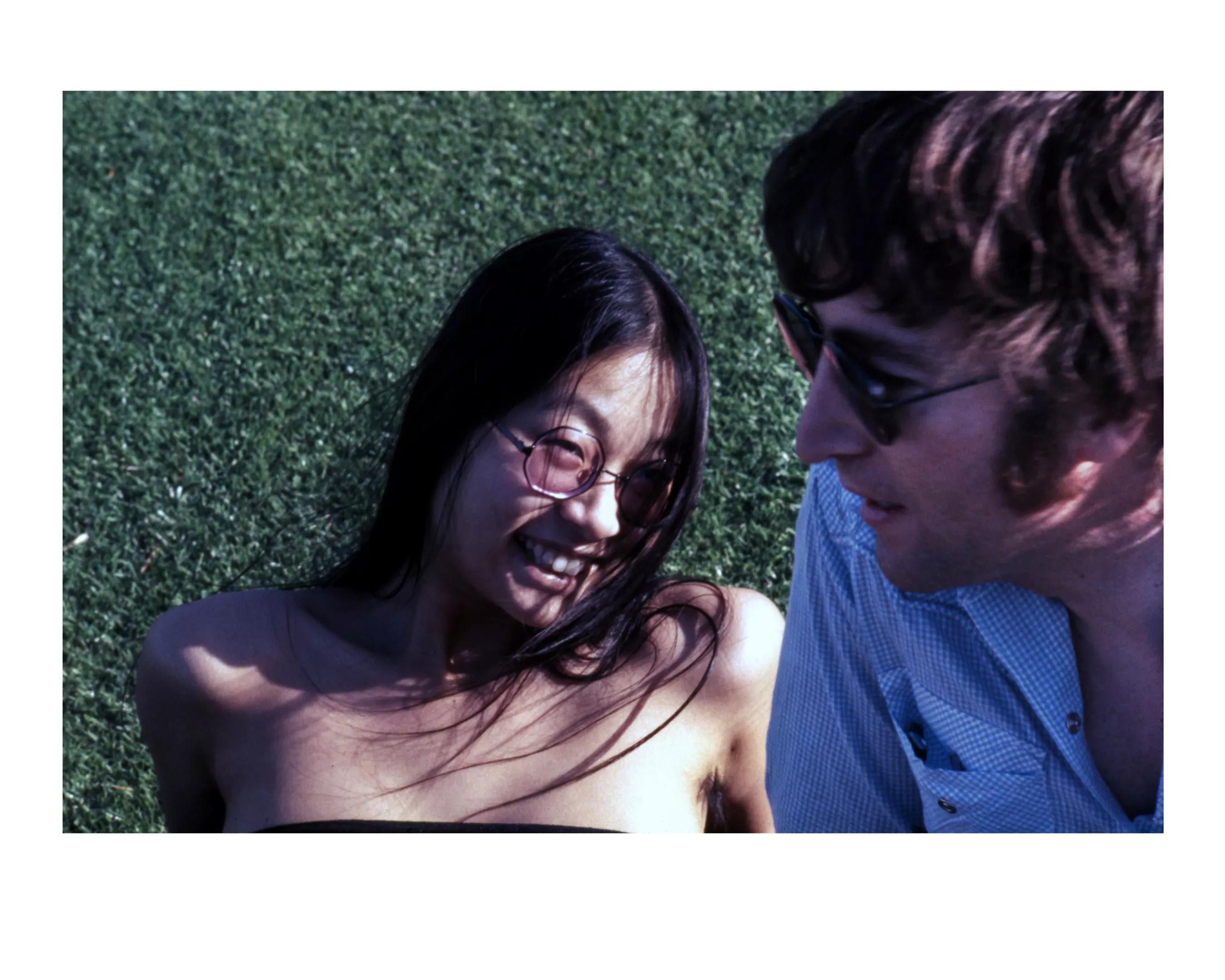 woman with black hair and sunglasses and man in white t-shirt and sunglasses smiling on the grass.