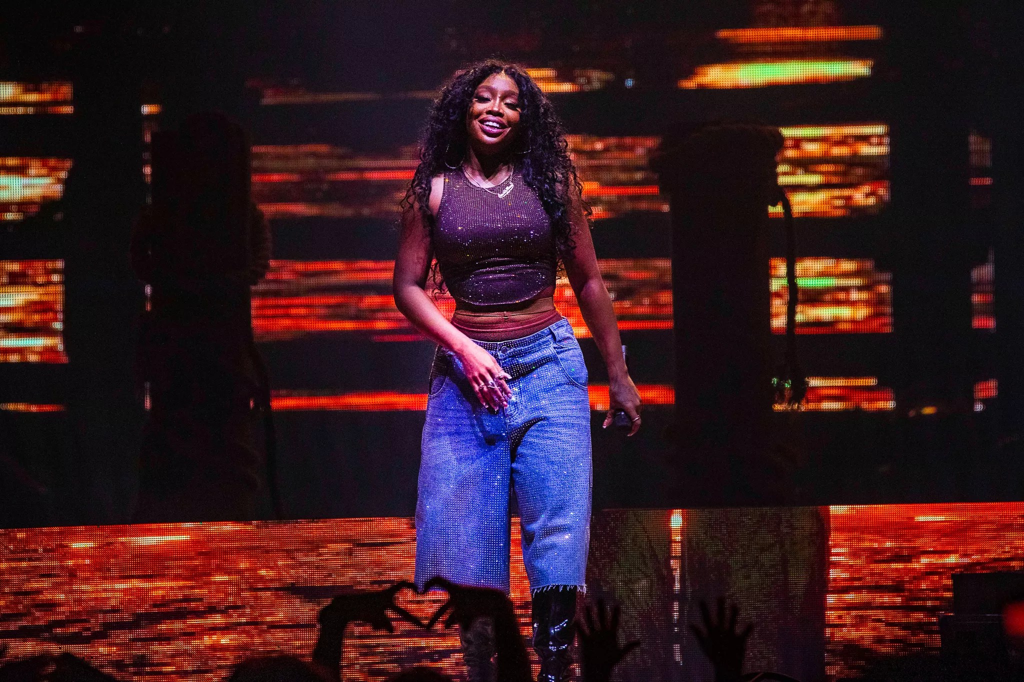 R&B singer SZA in blue pants on stage with an orange background