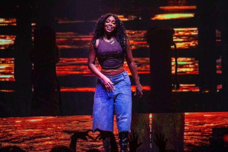 R&B singer SZA in blue pants on stage with an orange background