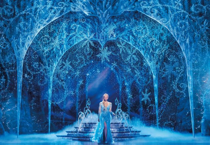 a woman in a blue dress on stage with ice decorations for Frozen production