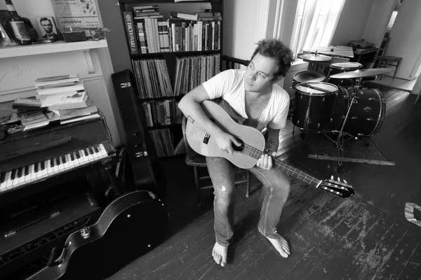 a black and white photo of a man sitting strumming his acoustic guitar