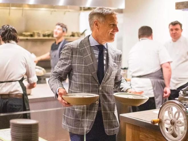 a man in a suit holding plates in a kitchen